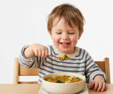 A smiling young child eating a bowl of vegetable soup.